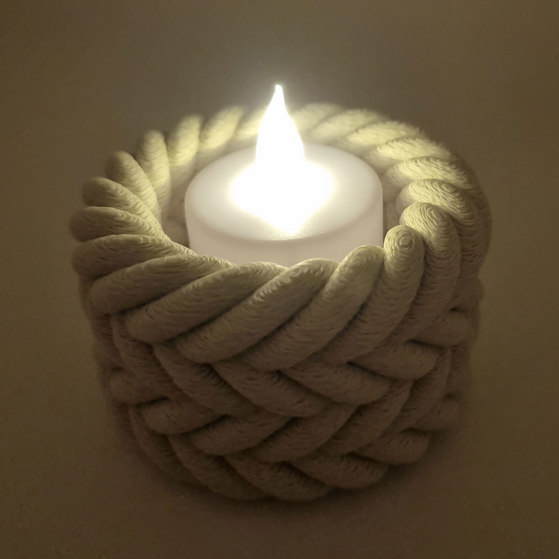 Beige flettet fyrfadsstage med tændt hvidt LED-lys.