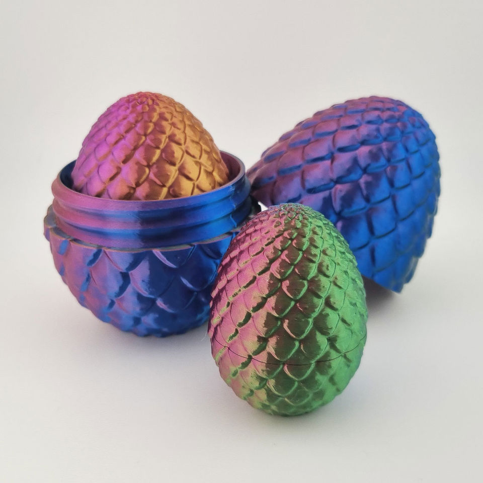 Tre flerfarvede 3D-printede drageæg med skælstruktur, ét åbent i to dele.