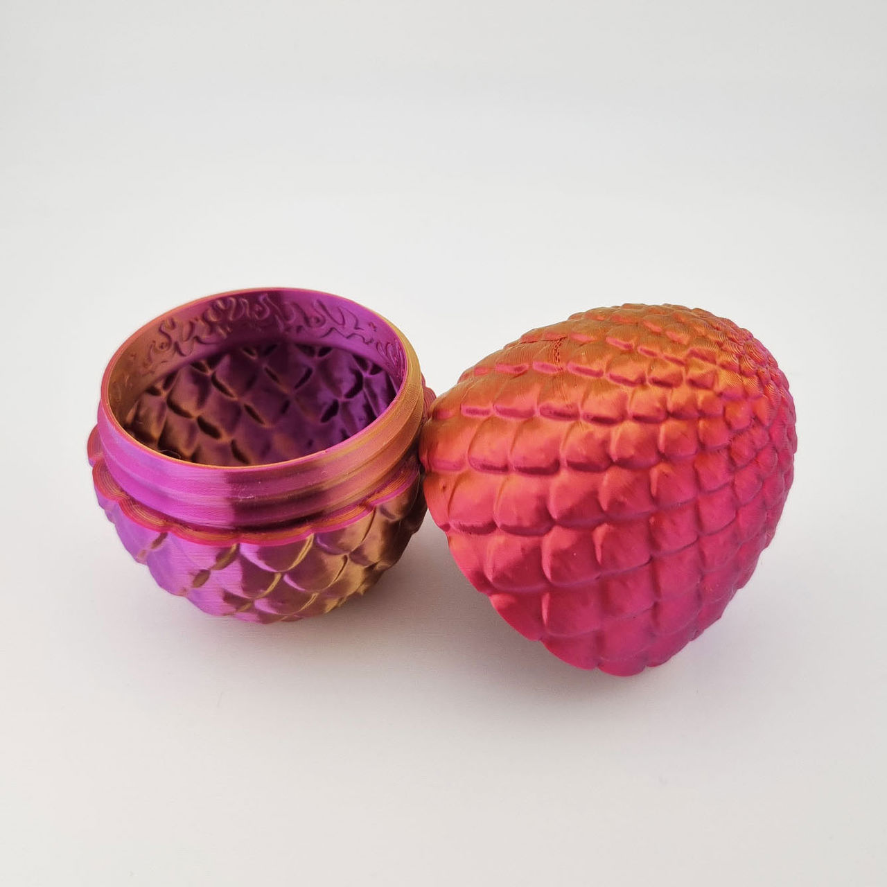 Pink-orange drageæg med skælstruktur, åbnet som todelt beholder.