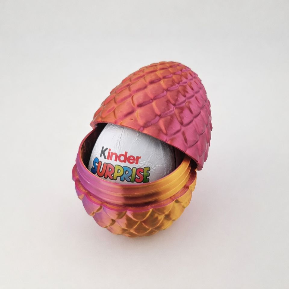 Pink-orange drageæg med skælstruktur, åbnet omkring et Kinder Surprise-æg.
