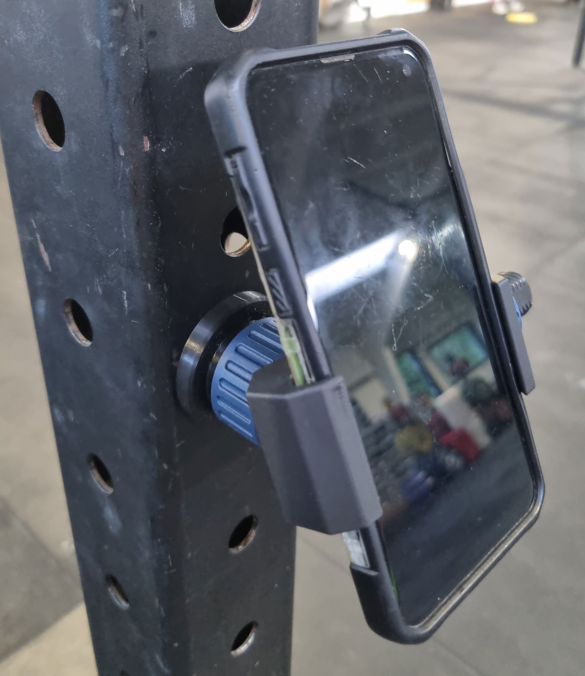 Sort magnetisk mobilholder med blå drejeknap monteret på perforeret metalstolpe.