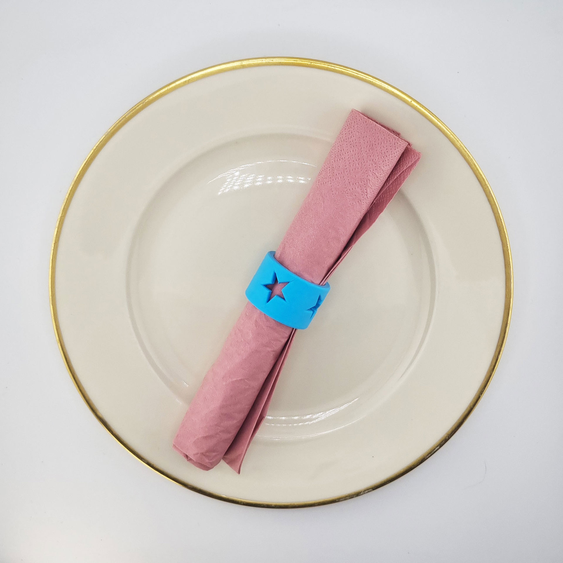 Blå servietring med stjerne omkring rosa serviet på hvid tallerken.