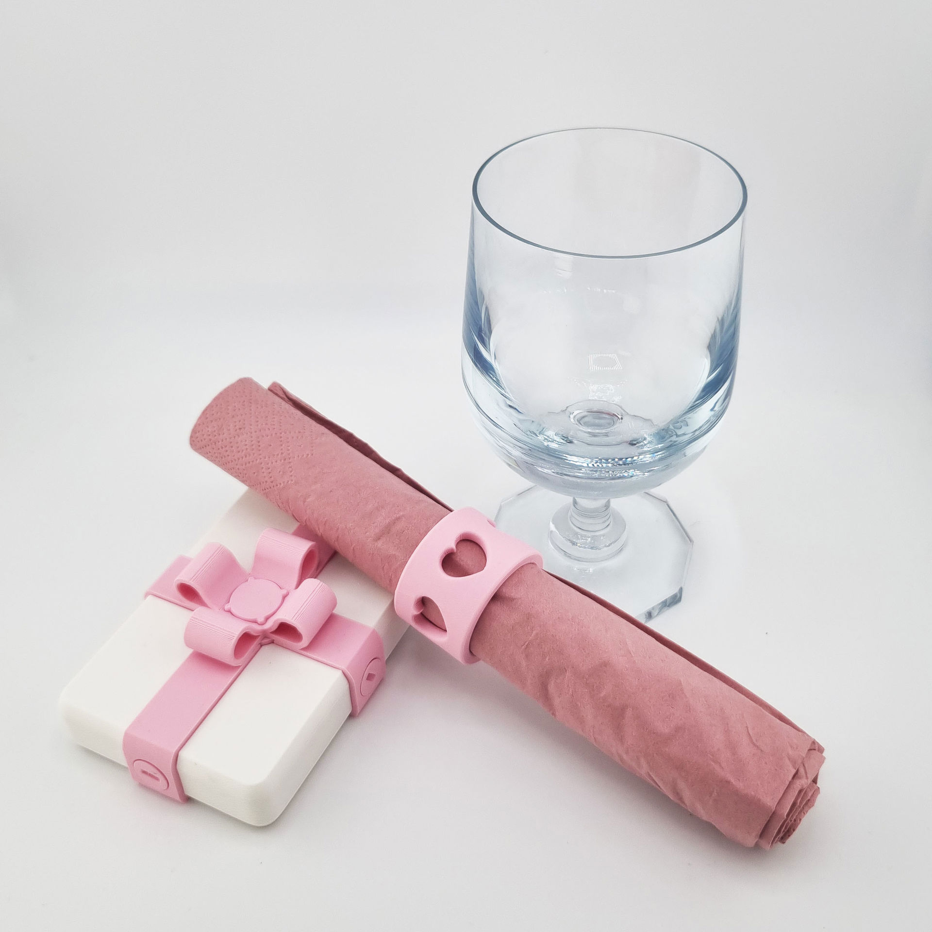 Rosa 3D-printet servietring med hjerter og gavebånd ved klart glas