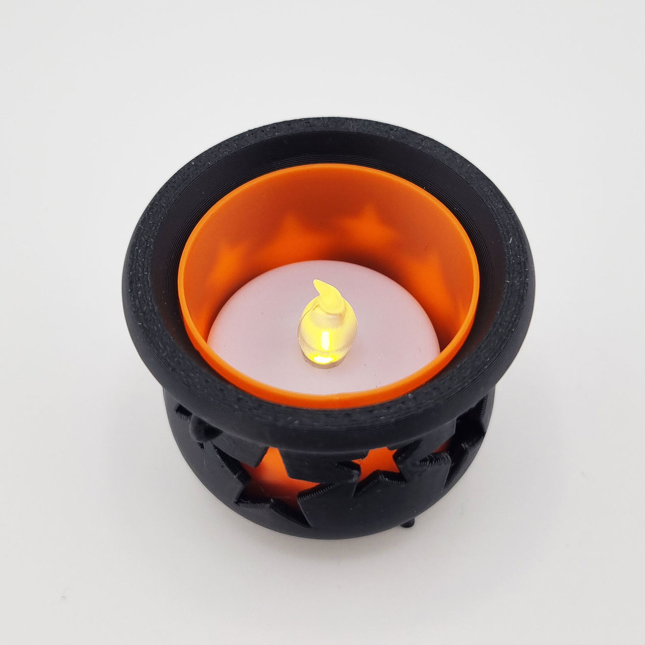 Sort heksekedel med orange inderside, stjerneudskæringer og hvidt LED-lys.