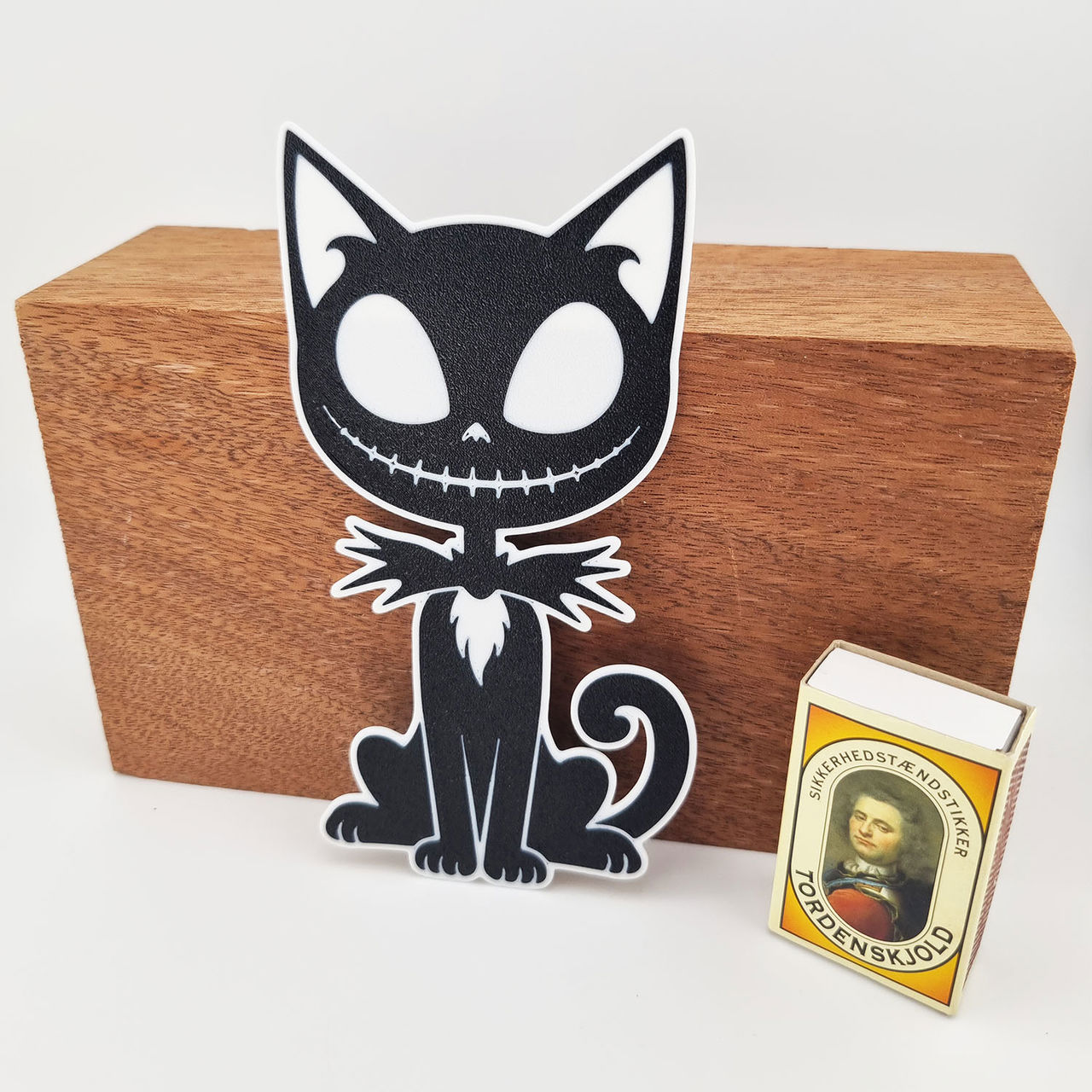 Sort-hvid 3D-printet kattefigur med store øjne, spidse ører og krøllet hale.