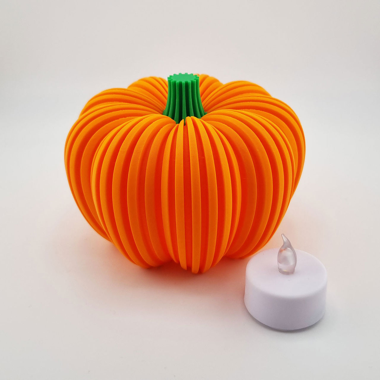 Orange ribbet græskar med grøn stilk og hvidt LED-fyrfadslys.