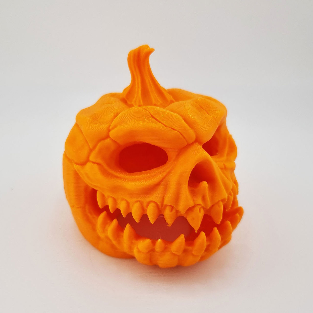 Orange 3D-printet græskarhoved med horn, tomme øjenhuler og spidse tænder.