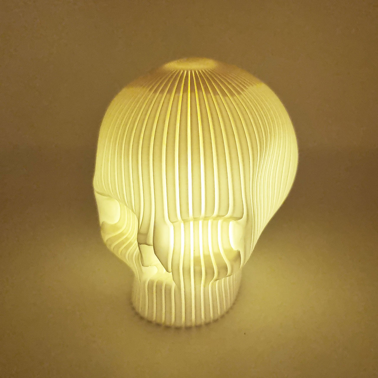 Hvid kranieformet lampe med varmt lys og lodrette lameller.