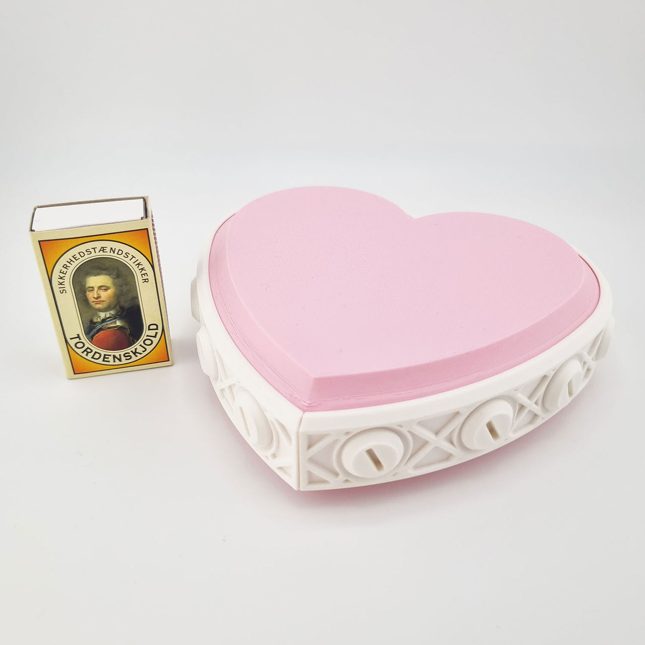 Hjerteformet gaveæske med rosa låg og hvid ramme med drejelåse.