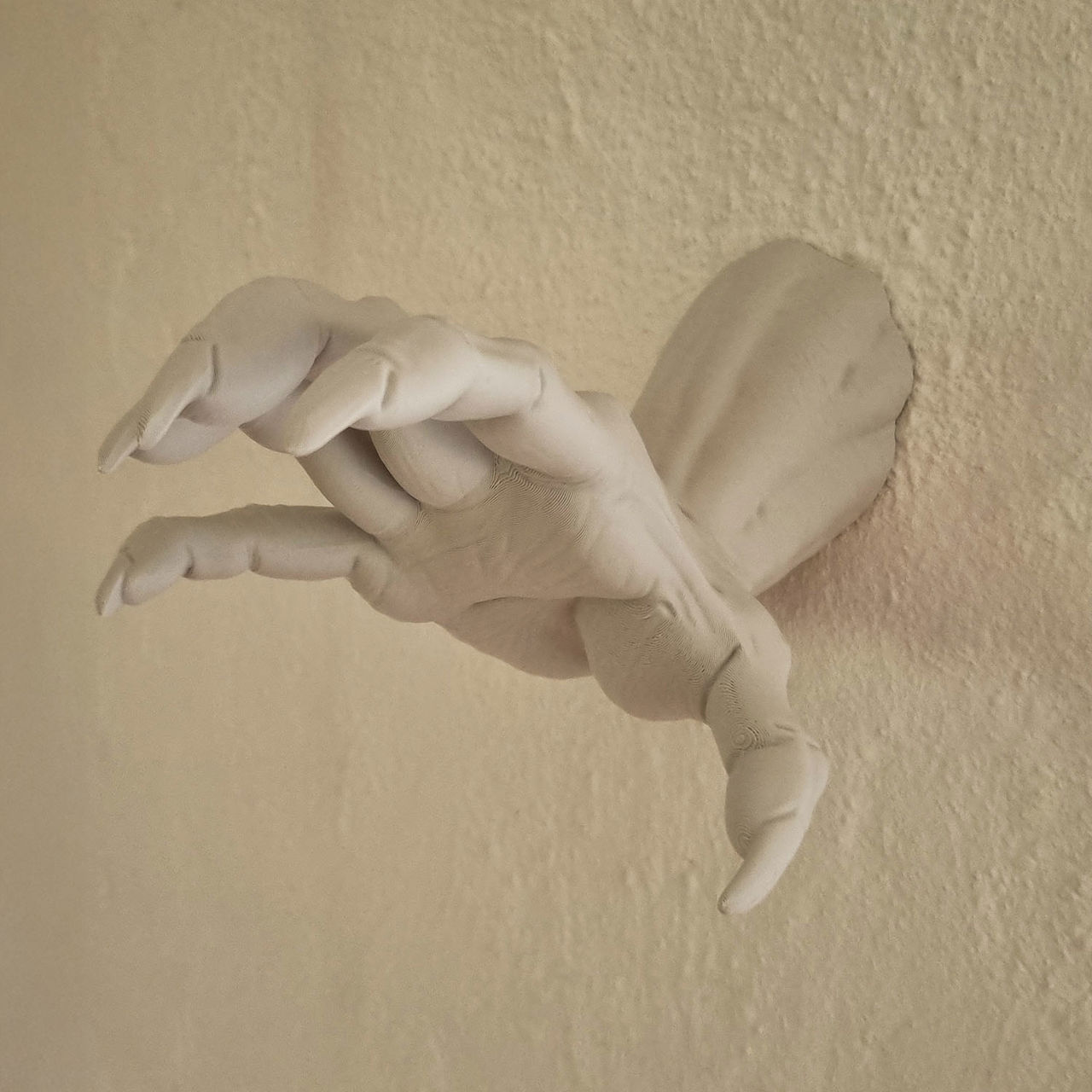 Hvid 3D-printet zombiehånd med krumme fingre monteret på væg.