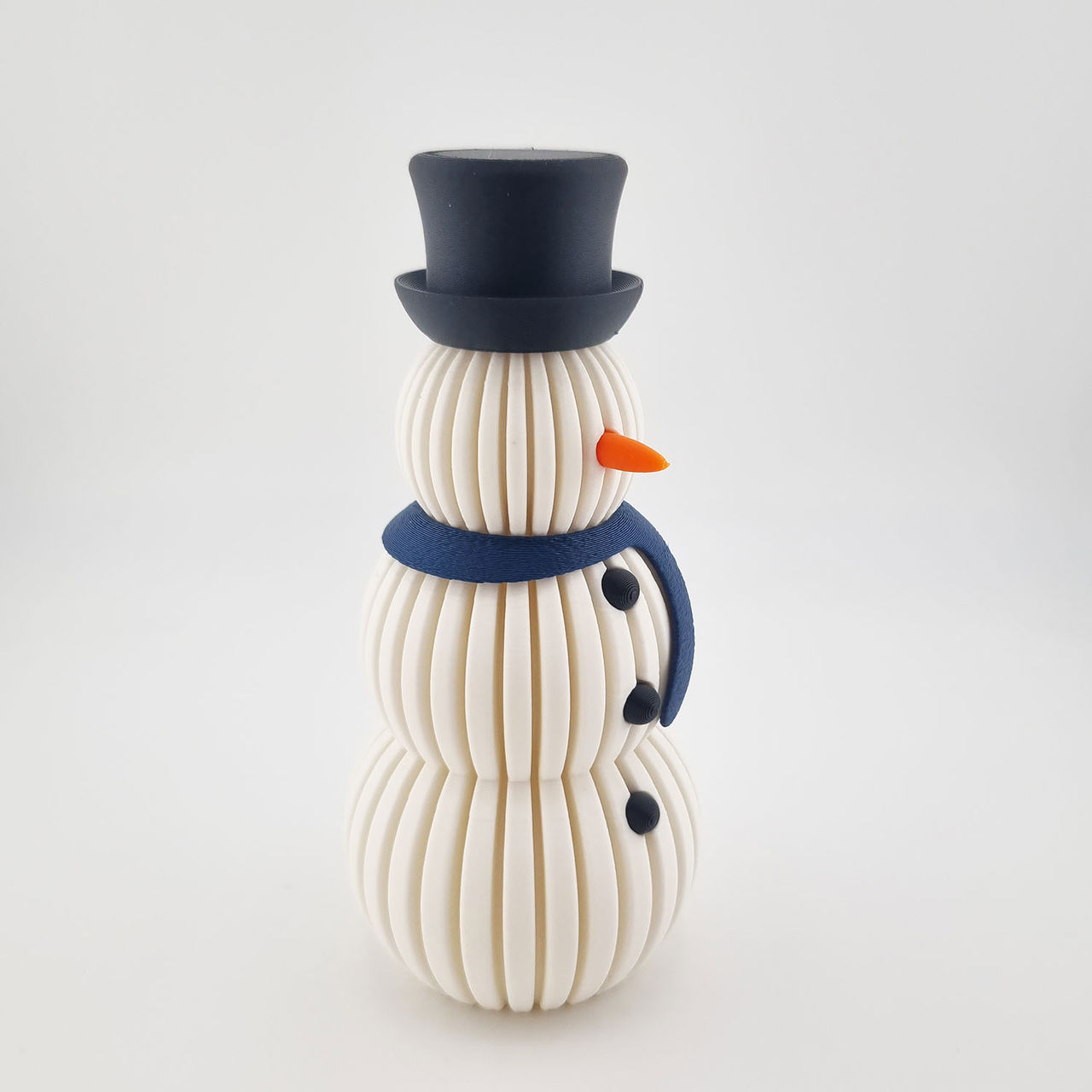 Hvid rillet 3D-printet snemand med sort hat, blå halstørklæde og orange næse.